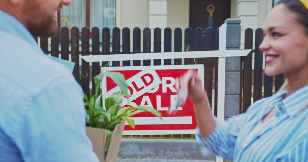 Young couple standing in front of sold sign looking at newly purchased home family mov SBI